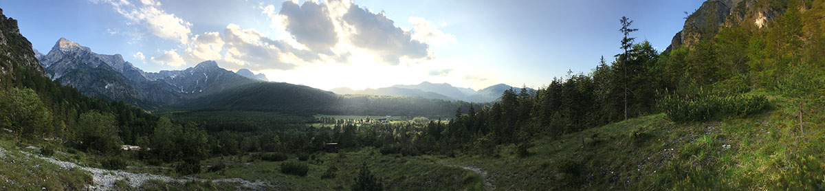 Kitschiger Ausblick auf das Tal in der Nähe des Almsees; Links sind hohe Berge zu sehen, in der Mitte das Tal und darüber geht die Sonne unter, rechts sind grüne Wälder und Wiesen zu sehen.