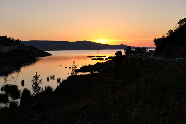 Abendstimmung, orangefarbener Sonnenuntergang, Blick von einer Einbuchtung mit Wasserpflanzen Richtung Meer, wobei im Hintergrund Inseln zu sehen sind