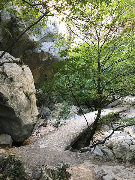 Ein Weg der über Felsen, durch Laubbäume und neben großen abgerundeten Felsen bzw. Steinen führt